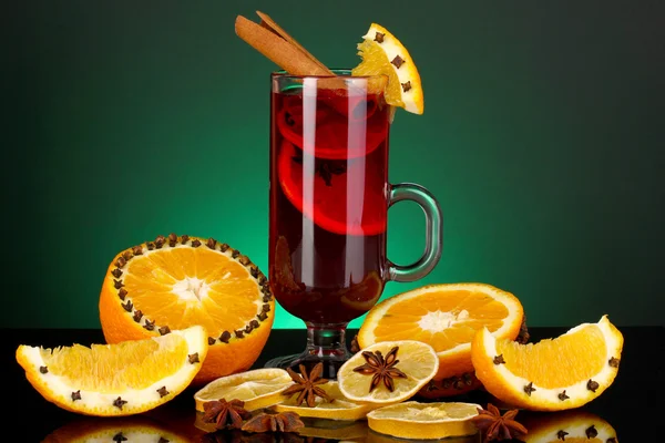 Fragrant mulled wine in glass with spices and oranges around on green background — Stock Photo, Image