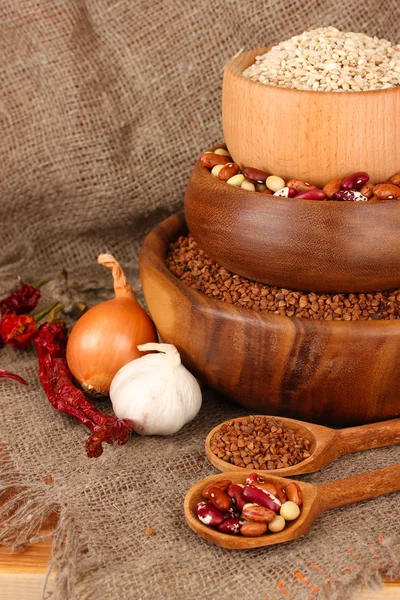 Ruwe tarwe, boekweit en bonen in houten kommen op tafel op rouwgewaad achtergrond — Stockfoto