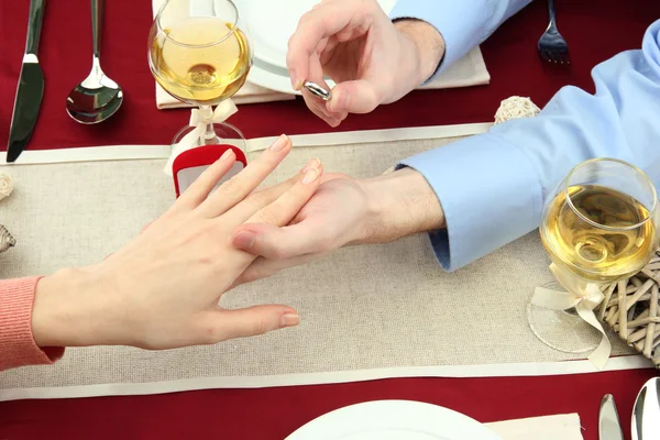 A man proposing and holding up an engagement ring over restaurant table — Stock Photo, Image