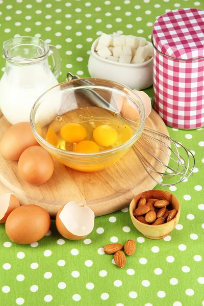 Broken egg in bowl and various ingredients next to them on green tablecloth close-up — Stock Photo, Image