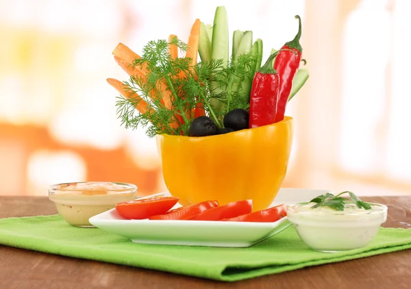 Diverse råa grönsaker pinnar i peppar skål på träbord på ljus bakgrund — Stockfoto