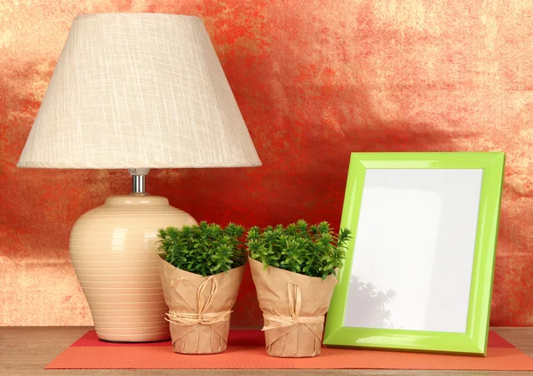 Marco de fotos colorido, lámpara y flores en la mesa de madera sobre fondo rojo — Foto de Stock