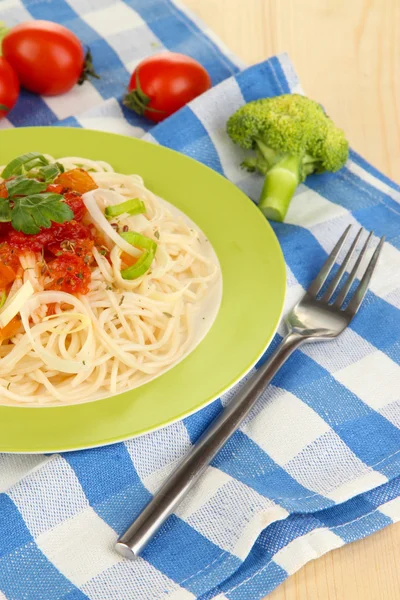 Välsmakande spaghetti med sås och grönsaker på tallriken på träbord närbild — Stockfoto