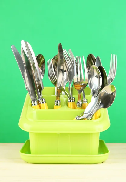 Knives, spoons, forks in plastic container for drying, on color background — Stock Photo, Image