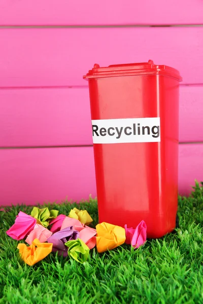 Recycling bin with papers on grass on pink background — Stock Photo, Image