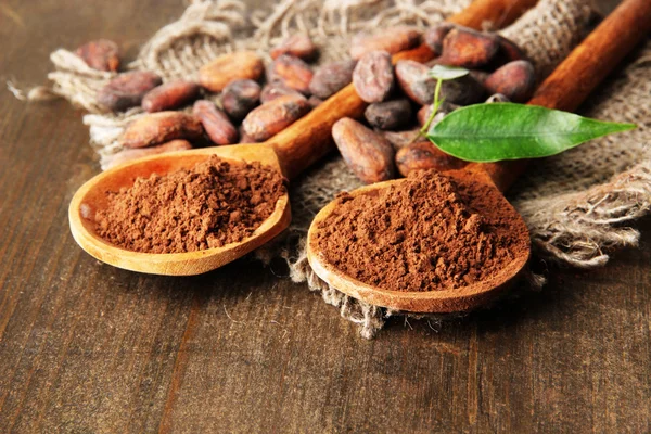 Cacaopoeder en bonen in lepels op houten achtergrond — Stockfoto