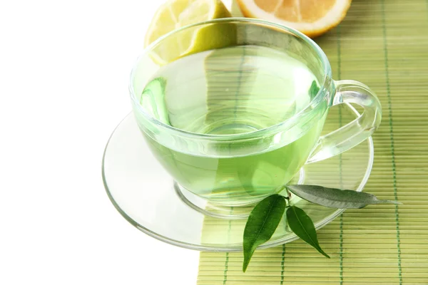 Taza transparente de té verde con limón en estera de bambú, aislado en blanco —  Fotos de Stock