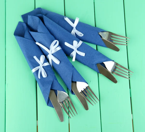 Вилки и ножи, завернутые в голубые бумажные салфетки, на фоне цвета дерева — стоковое фото