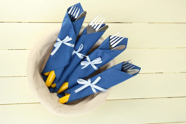 Forks and knives wrapped in blue paper napkins, on color wooden background — Stock Photo, Image