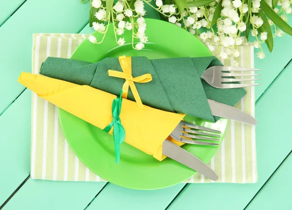Çatal ve bıçaklar renk ahşap zemin üzerine yeşil ve sarı kağıt peçete sarılmış — Stok fotoğraf