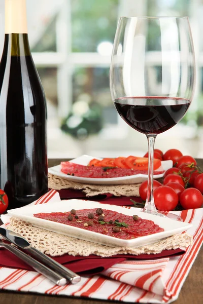 Tasty salami on plates on wooden table on window background — Stock Photo, Image