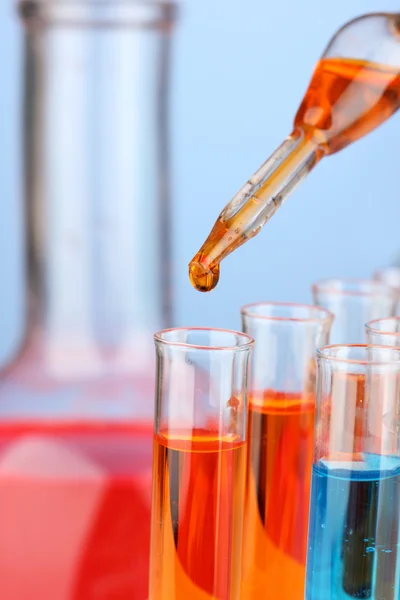 Pipeta de laboratorio con gota de líquido de color sobre tubos de ensayo de vidrio, primer plano — Foto de Stock