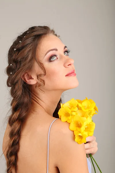 Jovem com belo penteado e flores, em fundo cinza — Fotografia de Stock