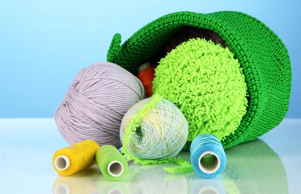 Colorful yarn for knitting in green basket on blue background — Stock Photo, Image