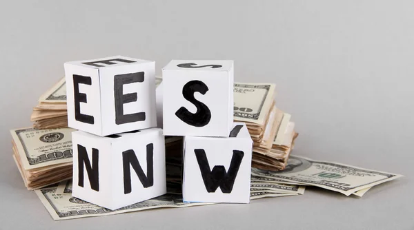 Cubos de papel branco rotulado "Notícias" com dinheiro em fundo cinza — Fotografia de Stock