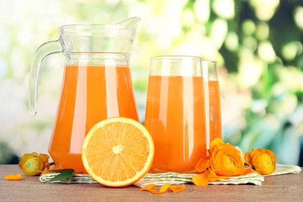 Bicchieri e brocca di succo d'arancia su tavolo di legno, su sfondo verde — Foto Stock