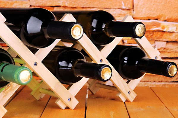 Ahşap stand taş duvar arka plan üzerine yerleştirilen şarap şişeleri — Stok fotoğraf