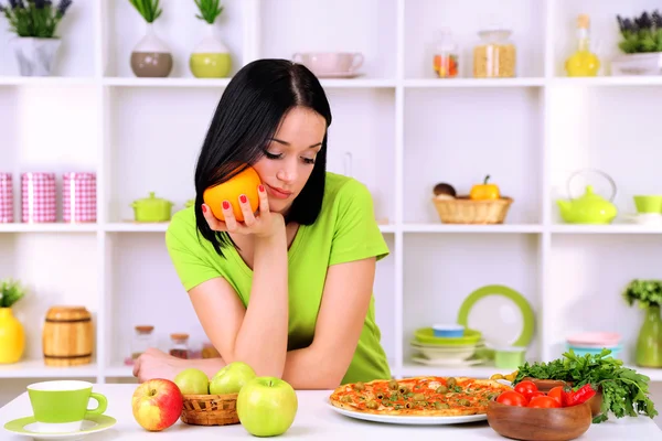 Mooi meisje selecteert pizza of dieet op keuken achtergrond — Stockfoto