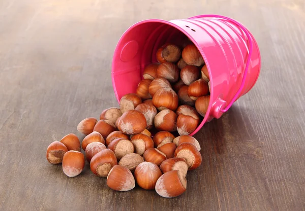 Overturned bucket with hazelnuts on wooden background — Stock Photo, Image