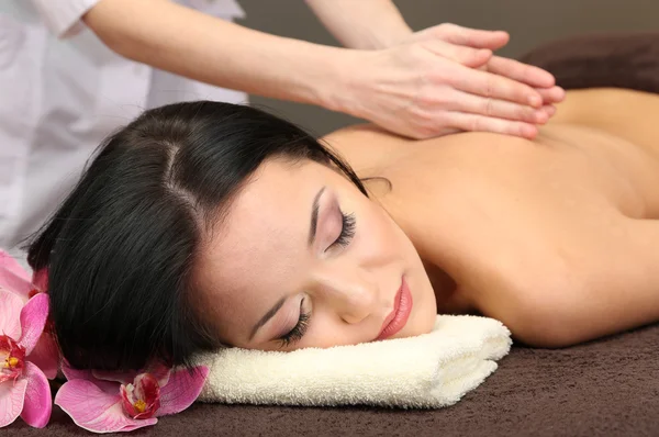 Schöne junge Frau im Wellness-Salon bekommt Massage mit Wellness-Steinen, auf dunklem Hintergrund — Stockfoto