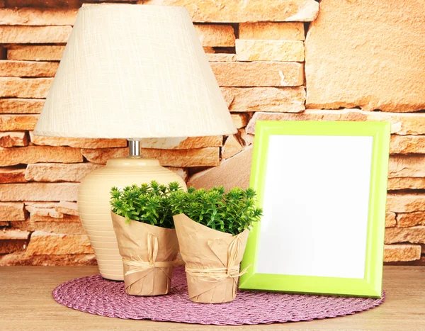 Marco de fotos colorido, lámpara y flores en la mesa de madera sobre fondo de pared de piedra — Foto de Stock