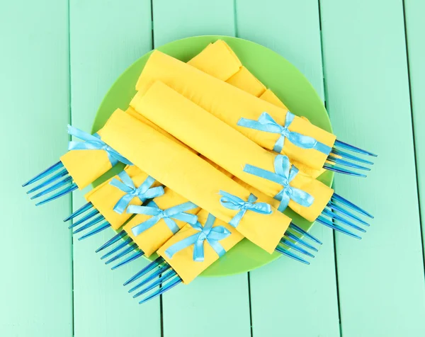 Blue plastic forks wrapped in yellow paper napkins, on color wooden background — Stock Photo, Image