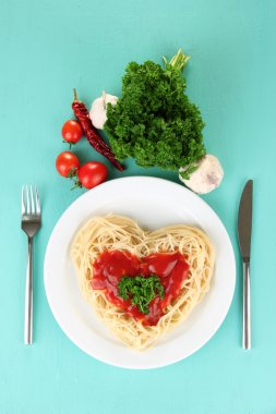 pişmiş spagetti dikkatle kalp şeklinde düzenlenmiş ve mavi zemin üzerine domates sosu ile tepesinde
