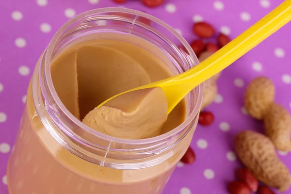 Köstliche Erdnussbutter in offener Bank auf lila Hintergrund mit Tupfen Nahaufnahme — Stockfoto