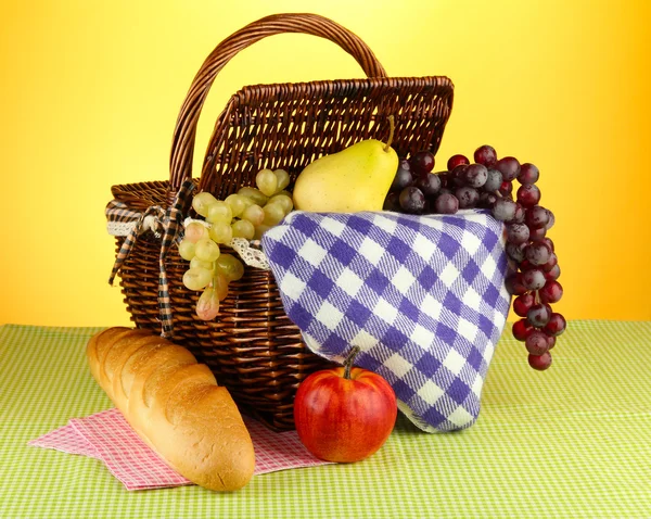 Picnic basket with fruits on cloth on yellow background — Stock Photo, Image