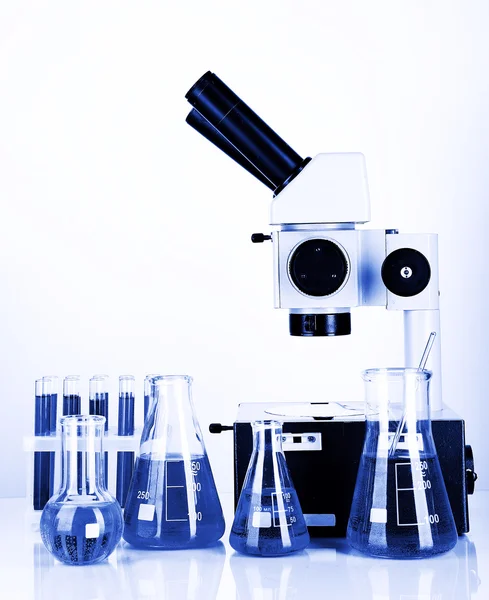 Reagenzgläser mit bunten Flüssigkeiten und Mikroskop im blauen Licht — Stockfoto