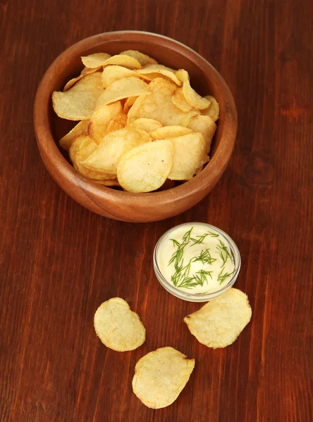 Potato chips in wooden bowl and sauce, on wooden background — Stock Photo, Image