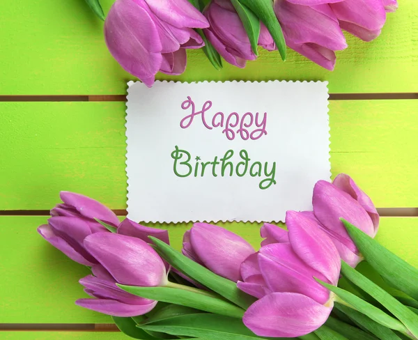 Beautiful bouquet of purple tulips and card on green wooden background — Stock Photo, Image