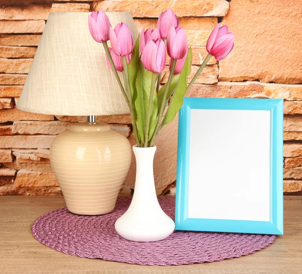 Marco de fotos colorido, lámpara y flores en la mesa de madera sobre fondo de pared de piedra — Foto de Stock