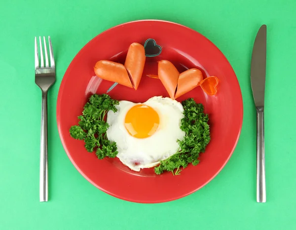 Sausages in form of hearts, scrambled eggs and parsley, on color plate, on color background — Stock Photo, Image