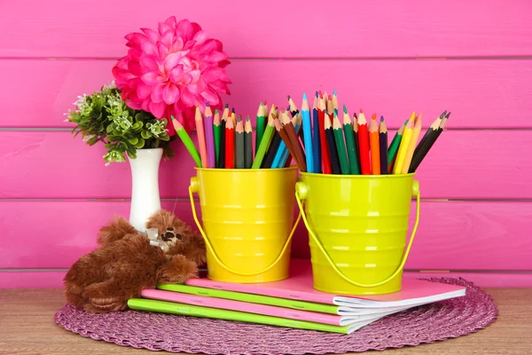 Lápis coloridos em pails com copybooks e urso na mesa sobre fundo rosa — Fotografia de Stock