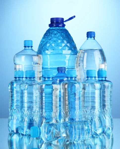 Różne butelki wody na niebieskim tle — Zdjęcie stockowe