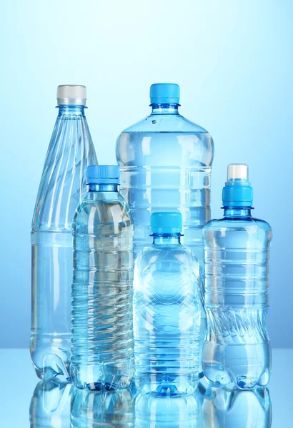 Diferentes botellas de agua sobre fondo azul — Foto de Stock