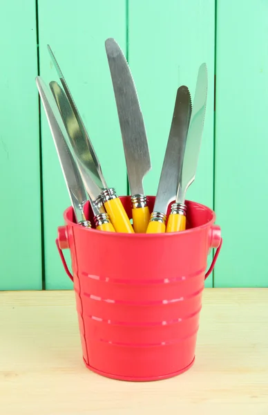 Messer in Metalleimer auf farbigem Holzhintergrund — Stockfoto