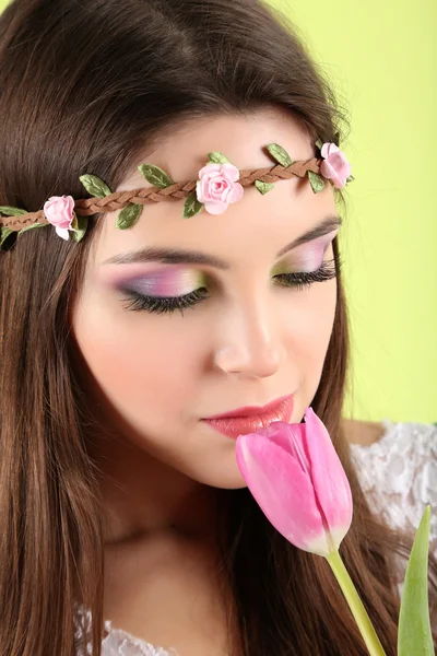 Young beautiful girl in decorative wreath with tulip in her hand, on green background — Stock Photo, Image