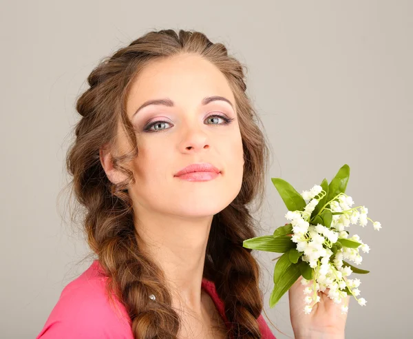 Młoda kobieta z piękną fryzurę i kwiaty, na szarym tle — Zdjęcie stockowe