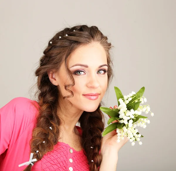 Mujer joven con hermoso peinado y flores, sobre fondo gris —  Fotos de Stock