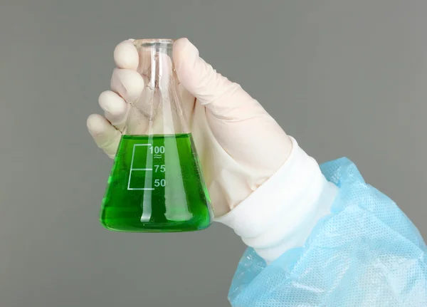 Glass tube with fluid in scientist hand during medical test on grey background — Stock Photo, Image