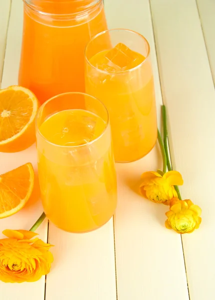 Vasos y jarra de zumo de naranja sobre fondo de madera blanca — Foto de Stock