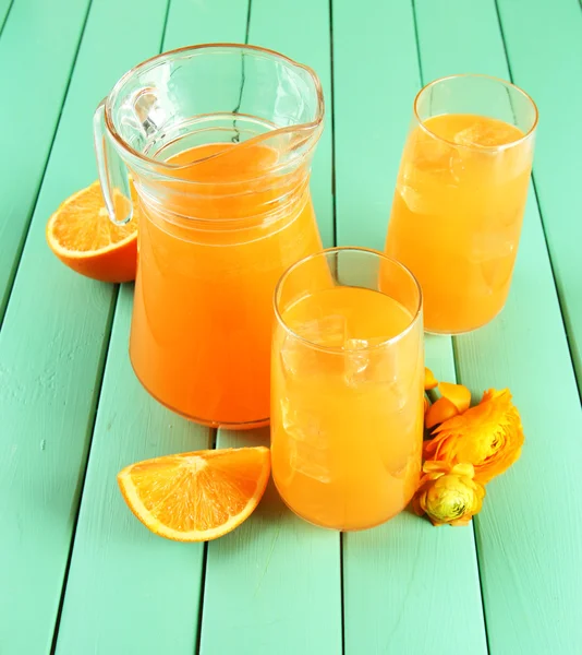 Glasögon och tillbringare med apelsinjuice på blå trä bakgrund — Stockfoto