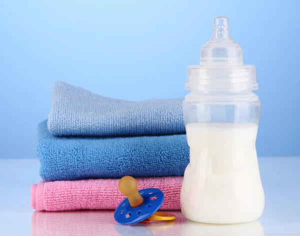 Bottle for milk with towels and nipple on blue background — Stock Photo, Image