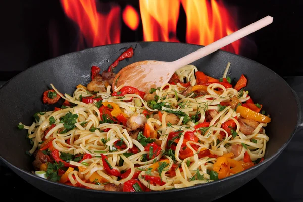 Noodles with vegetables on wok on fire background — Stock Photo, Image