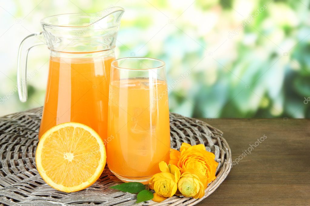 Glass and pitcher of orange juice on wooden table, on green background