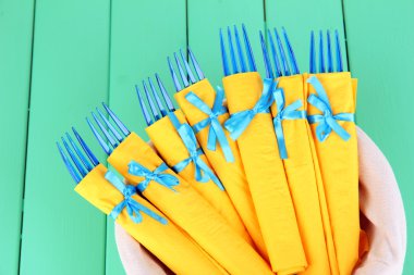 Sarı kağıt peçeteler, sepetteki renkli ahşap zemin üzerinde mavi plastik çatal sarılı