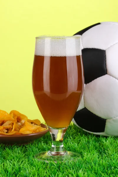 Copo de cerveja com bola de futebol na grama no fundo verde — Fotografia de Stock