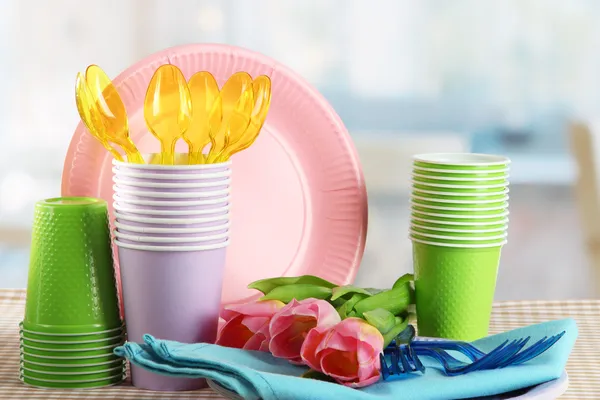 Multicolored plastic tableware on table with tulips close up — Stock Photo, Image